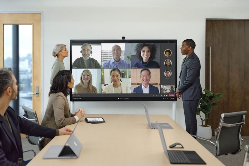 Two colleagues present at a Surface Hub 2S while on a Teams conference call with both in-person and remote team members.