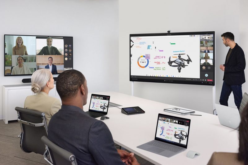 A presenter takes notes on a digital whiteboard on a Surface Hub 2S while meeting with in-person and remote teammates.