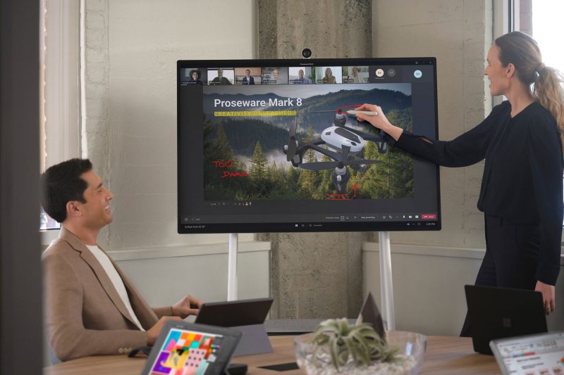 A presenter inks notes into PowerPoint Live on Surface Hub 2S while meeting with colleagues who in in-person and remote.