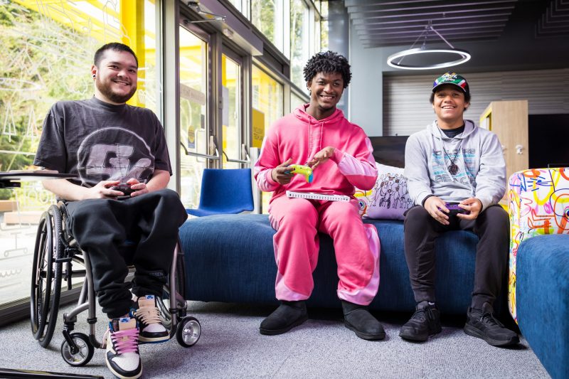 Three people sitting inside the Inclusive Tech Lab, holding gaming controllers