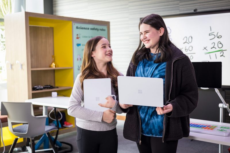 Two people standing inside the Inclusive Tech Lab; holding devices and smiling
