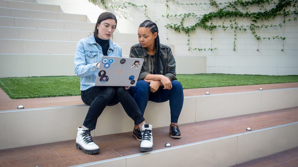 Two women sit outside working on a laptop