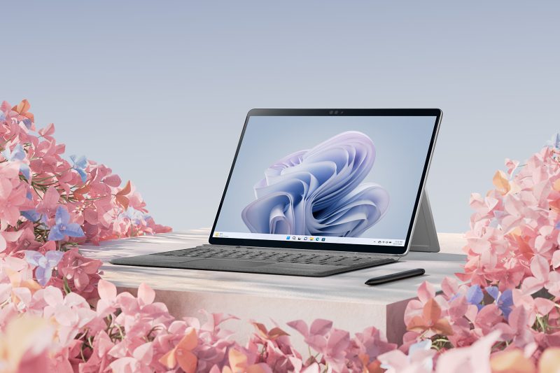 A detachable PC with keyboard and digital pen is surrounded by flowers.