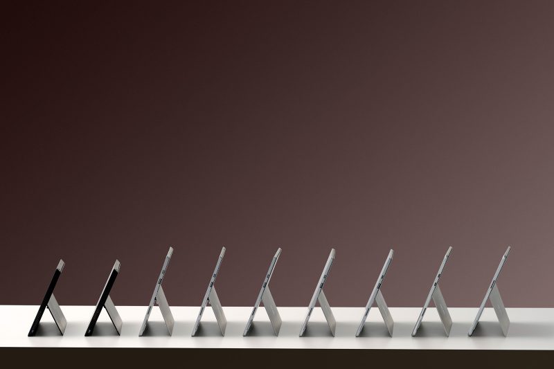 A series of nine tablet computers with kickstands are postioned next to each other on a table showing the ports located on their right sides.