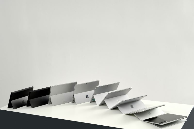 A series of nine tablet computers with kickstands are postioned next to each other on a table with each kickstand positioned slightly further back the the previous to create a wave effect.