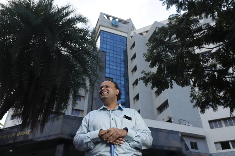 a man who is blind standing in front of SBI's office building