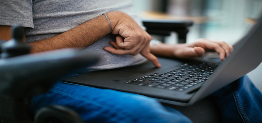Pratyush Nalam, a man who uses a wheelchair, puts his finger on the touchpad on a laptop. Accessibility, disability, and inclusion collection.