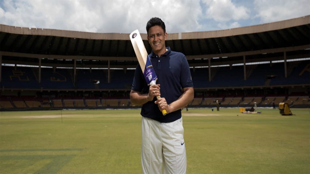 Anil Kumble holds a cricket bat in middle of field