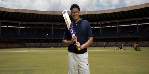 Anil Kumble holds a cricket bat in middle of field