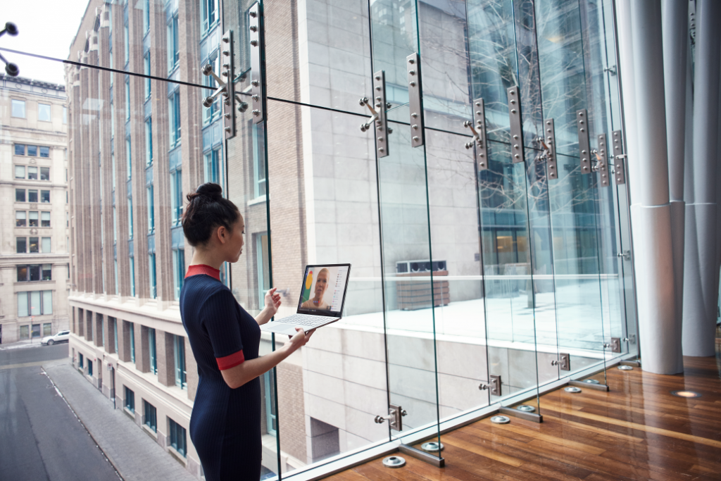 Female business professional standing in larger foyer while holding an open Dell device, running Microsoft Teams