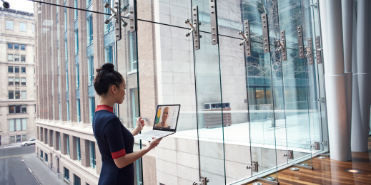 Female business professional standing in larger foyer while holding an open Dell device, running Microsoft Teams