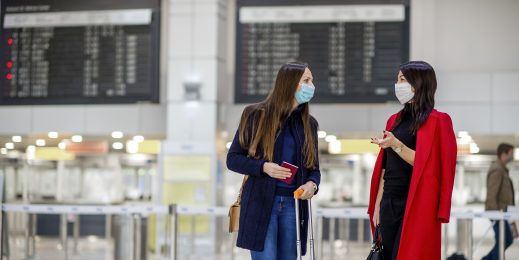 Young business women wearing protective face masks while waiting together in an airport lounge. Travel during pandemic.