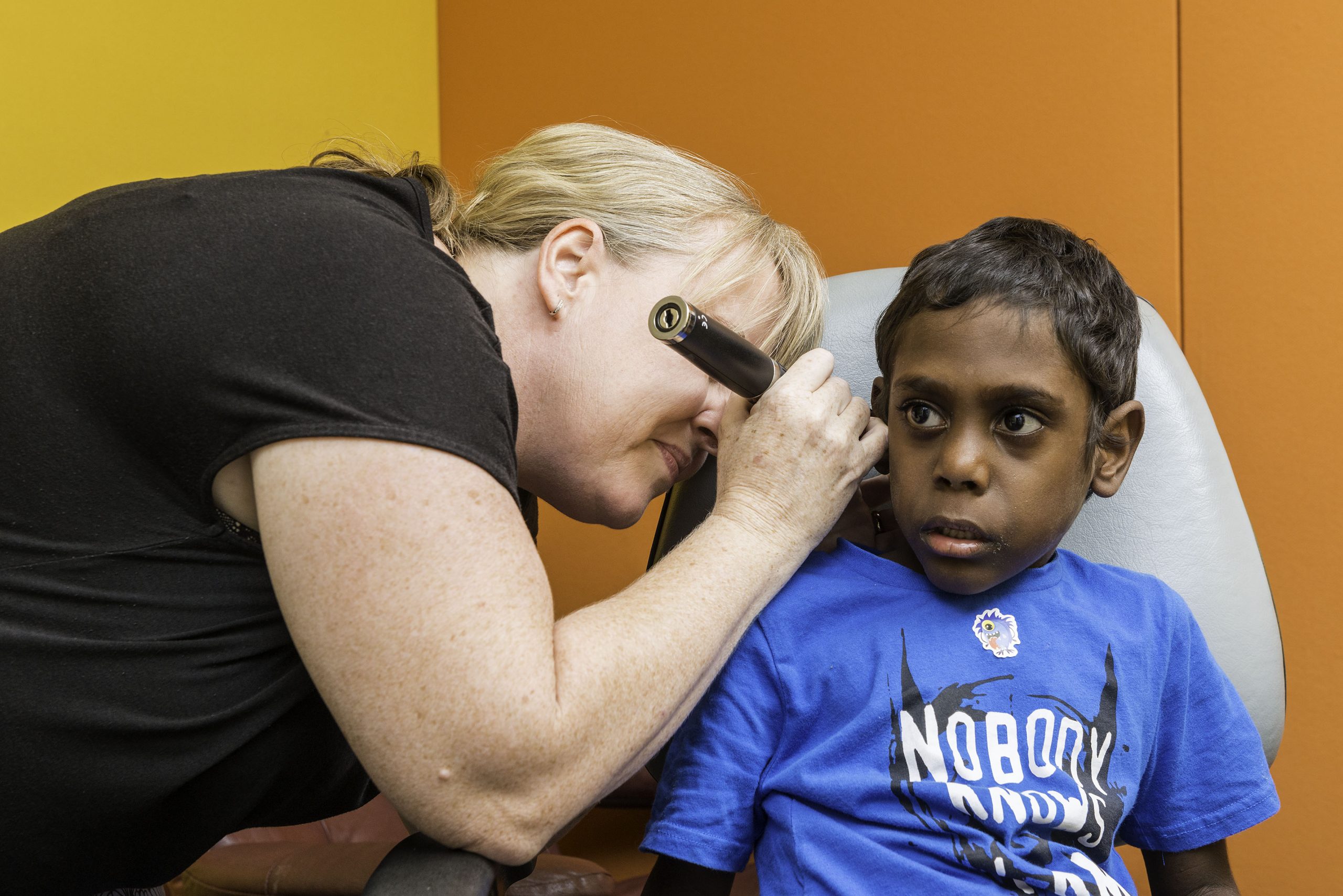 Adult female running an ear test exam for an Indigenous child
