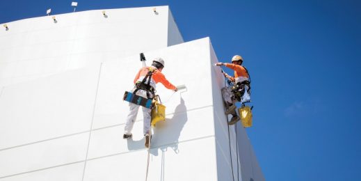 Two workers in safety gear harnessed in high ropes painting a tall building