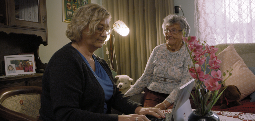 A nurse using a Surface Laptop, assisting an elderly patient