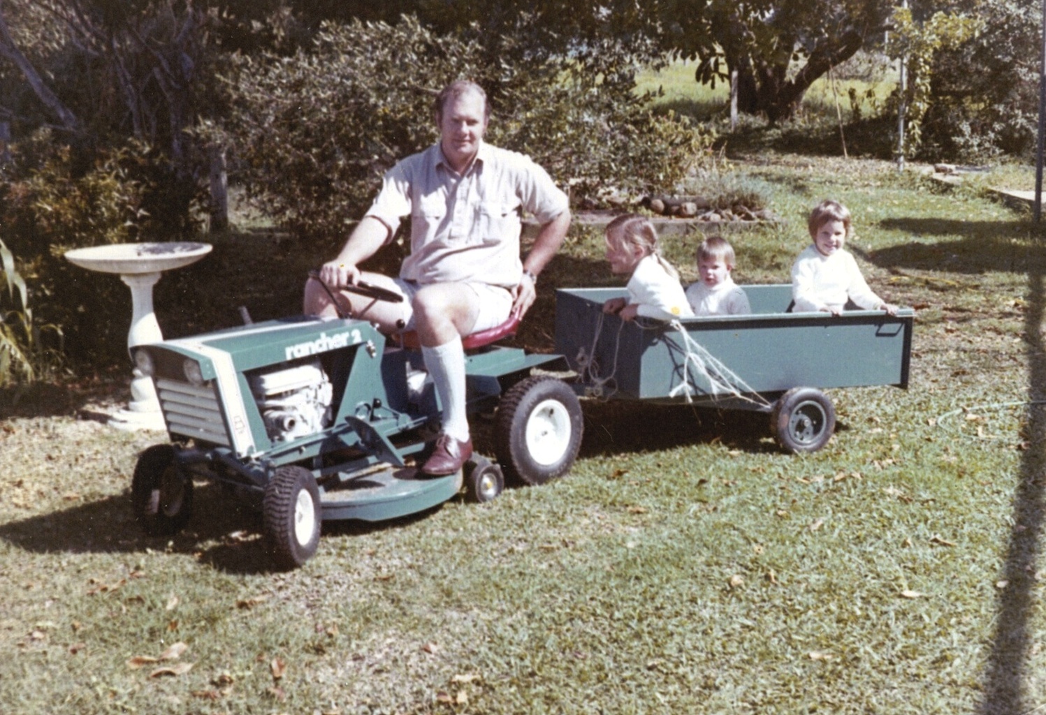 Old photograph of a dad driving a mower with two children