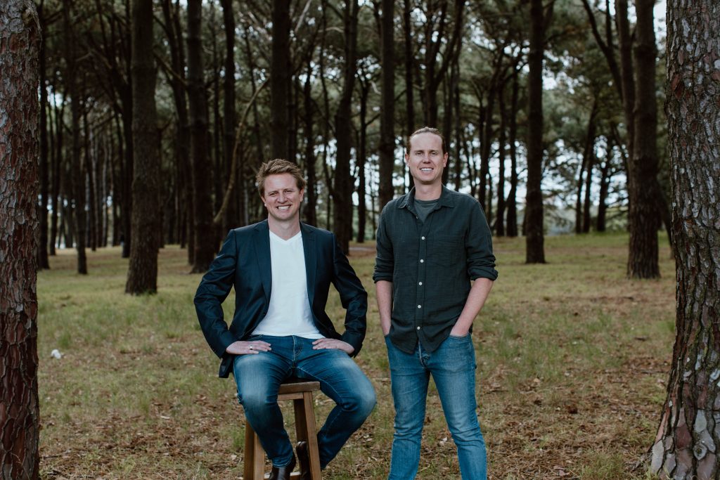 Two adult men standing in the middle of a forest