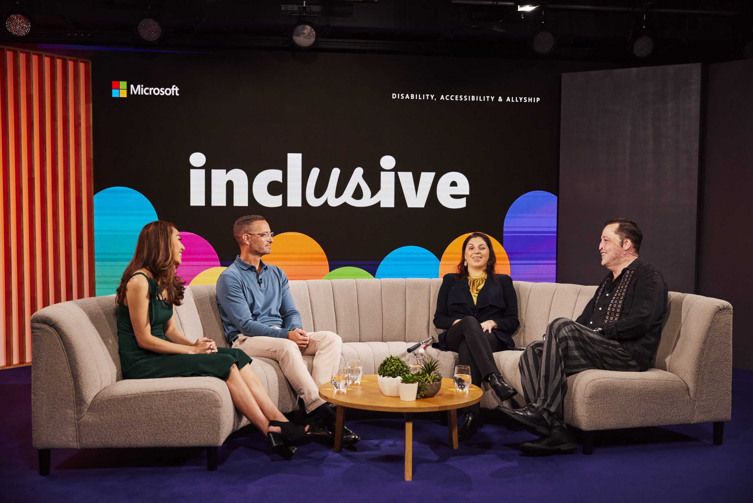 Group of four adults sitting on a biege couch infront of the Microsoft Inclusive event sign