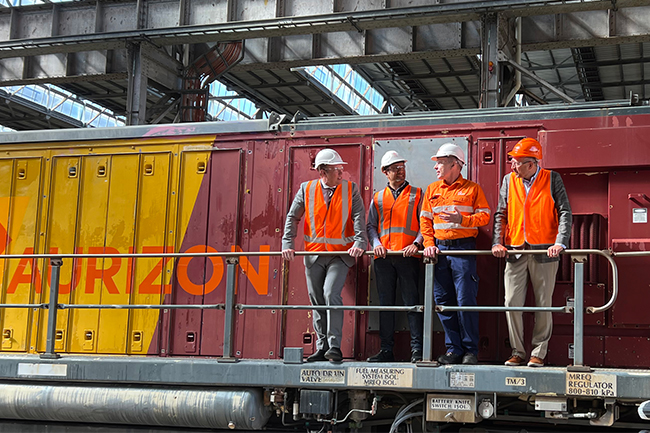 A group of adults wearing safety uniforms standing infront of a freight rail operator