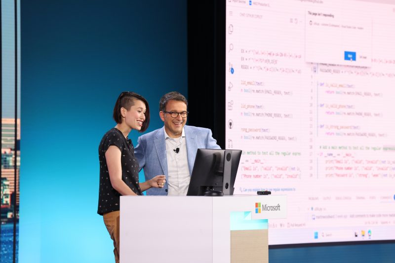 A man and a woman stand on stage behind a podium looking at a computer