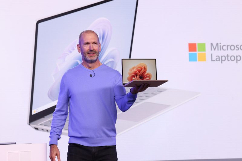 Image of Brett Ostrum, Microsoft corporate vice president for Surface devices, holding a Surface laptop while speaking on stage.