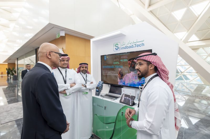 Three Saudi mean interacting with Microsoft Chairman and CEO Satya Nadella at an event booth