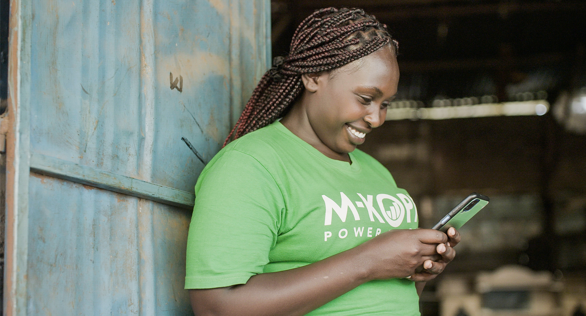 A woman in a green shirt smiles and looks at a cellphone