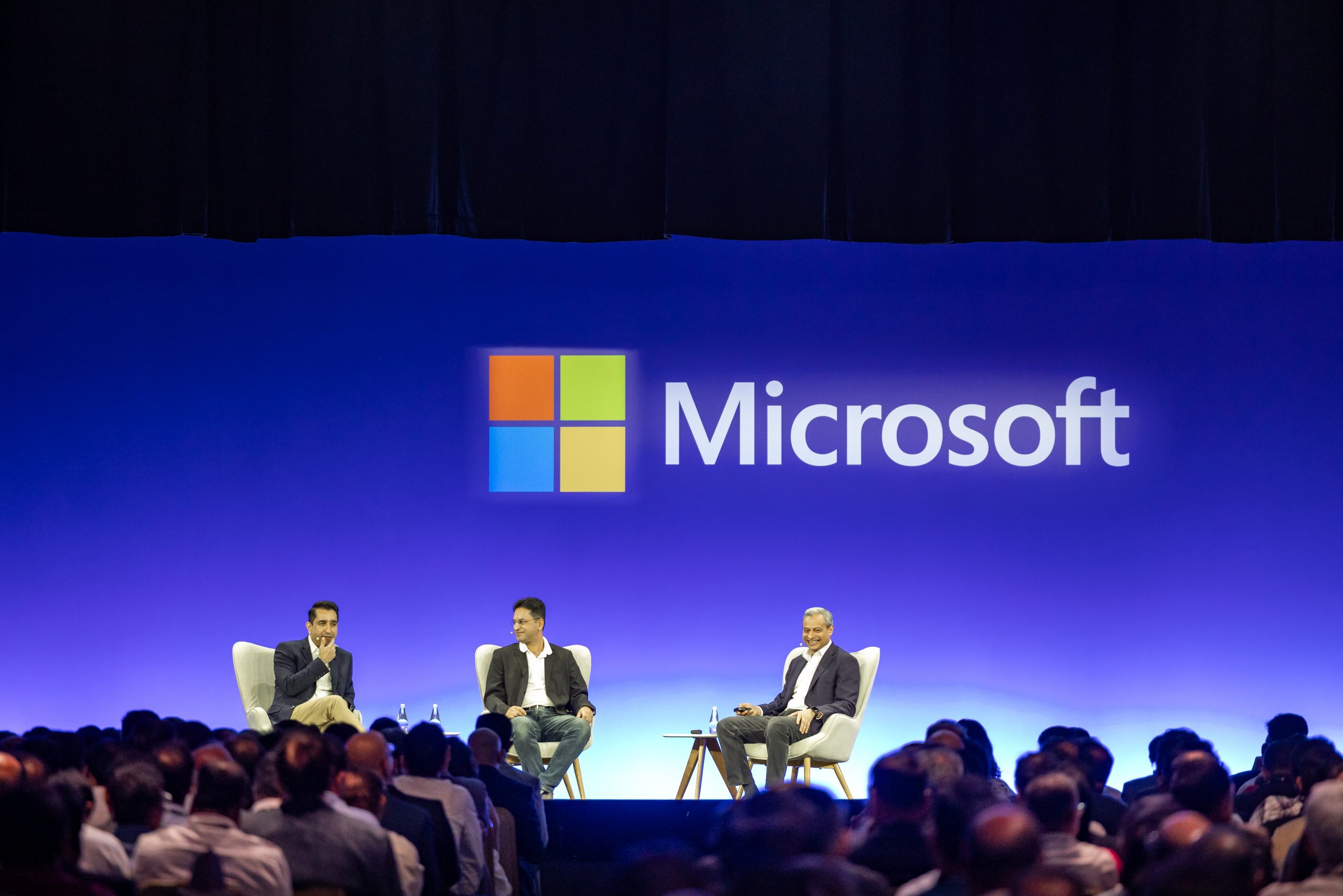 Three men in a panel on stage with Microsoft logo in the background