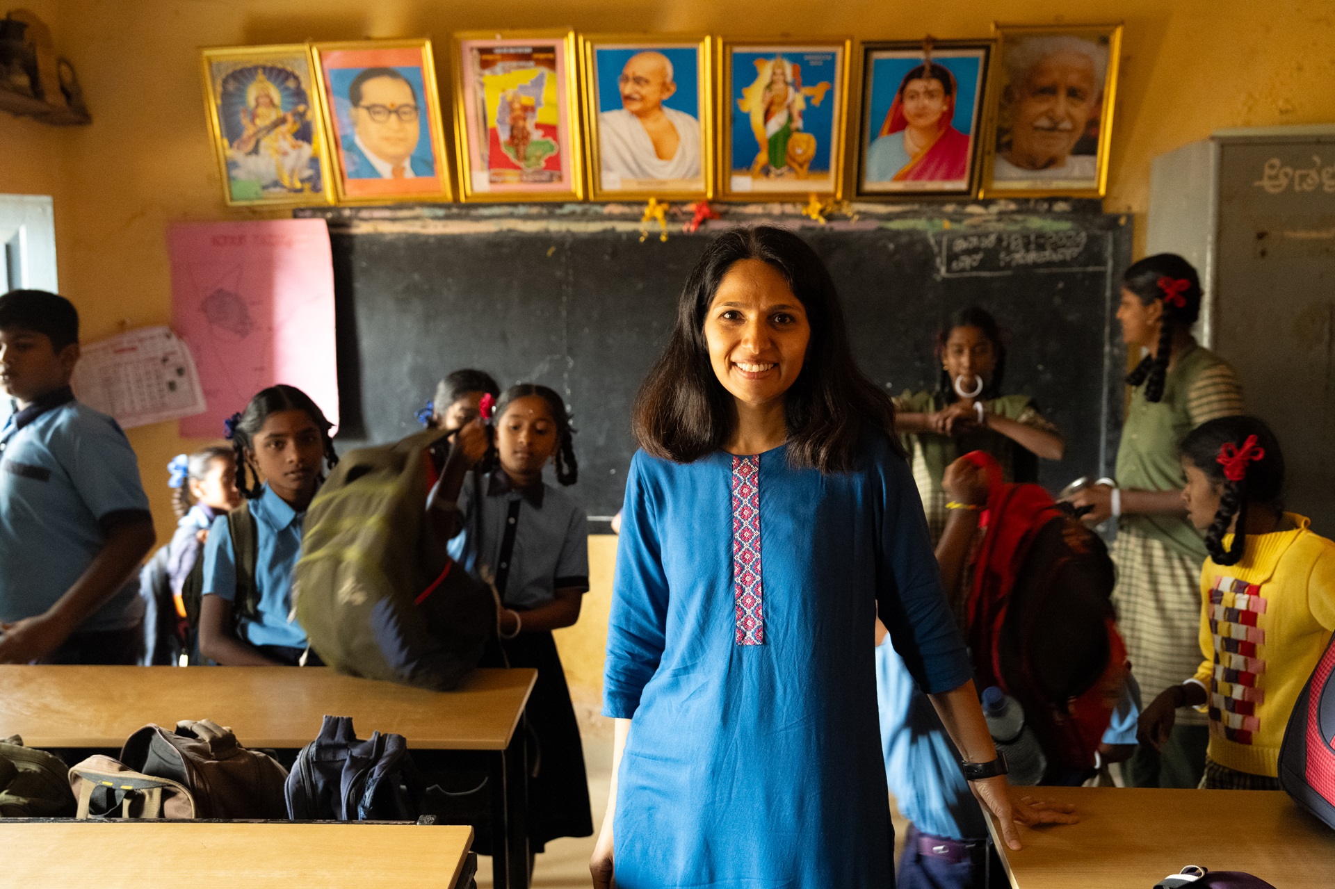A female NGO worker standing in a classroom with students in the background 