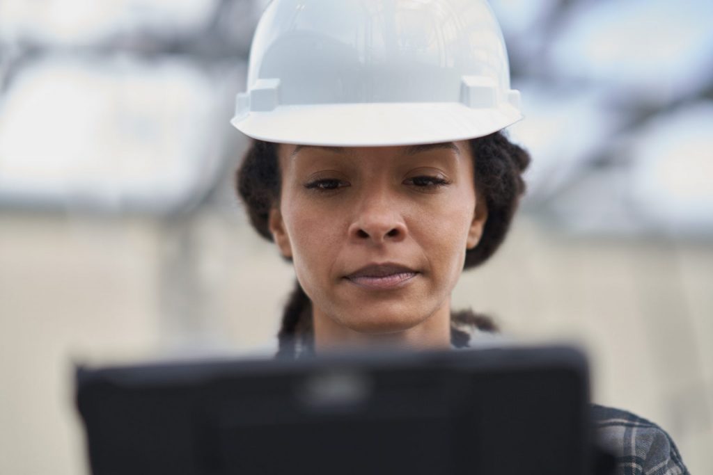 Woman stands in front of a computer with a hard hat on