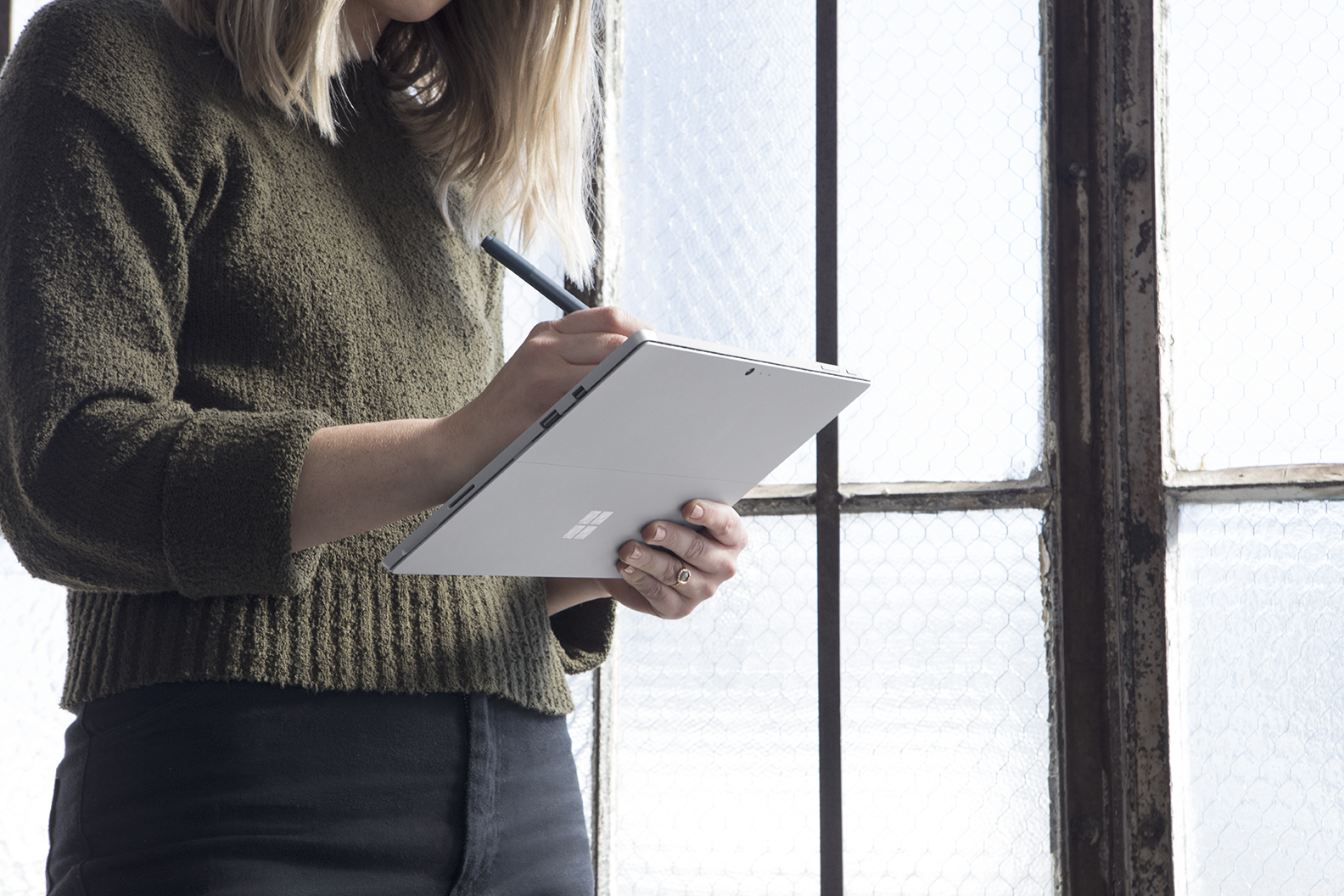 Woman standing up by window using Microsoft Surface device and Pen