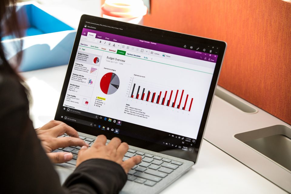 man typing on Surface laptop, with graphs on screen