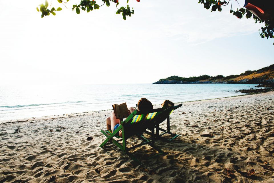 two people sitting in deckchairs on a sandy beach, reading books