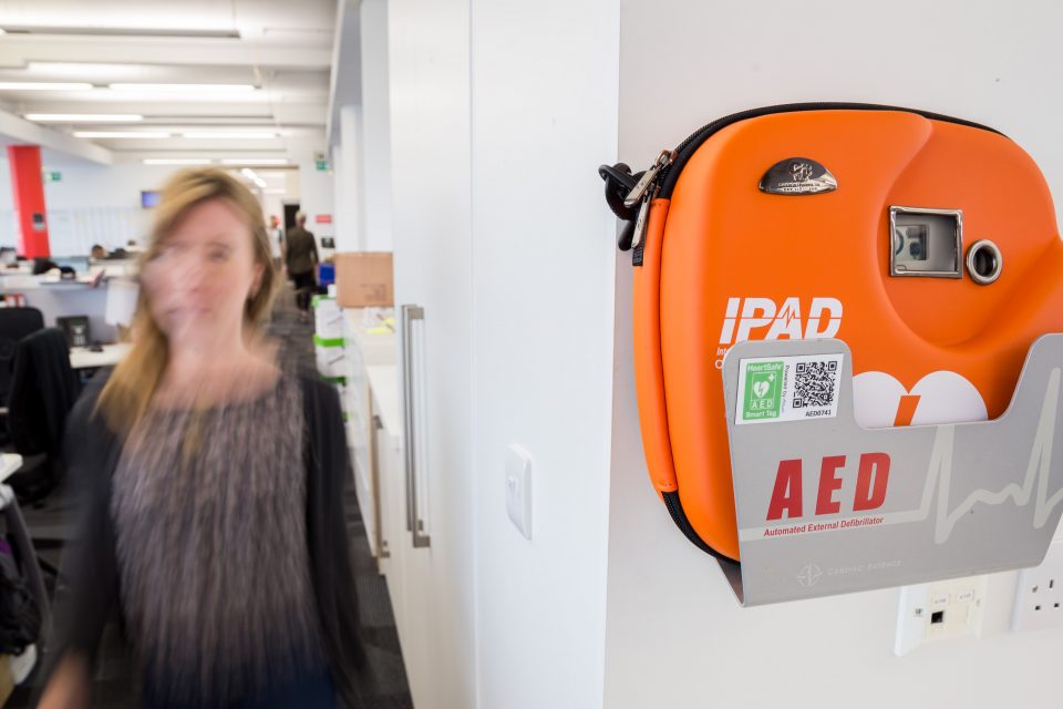 A woman walks past a defibrillator on a wall