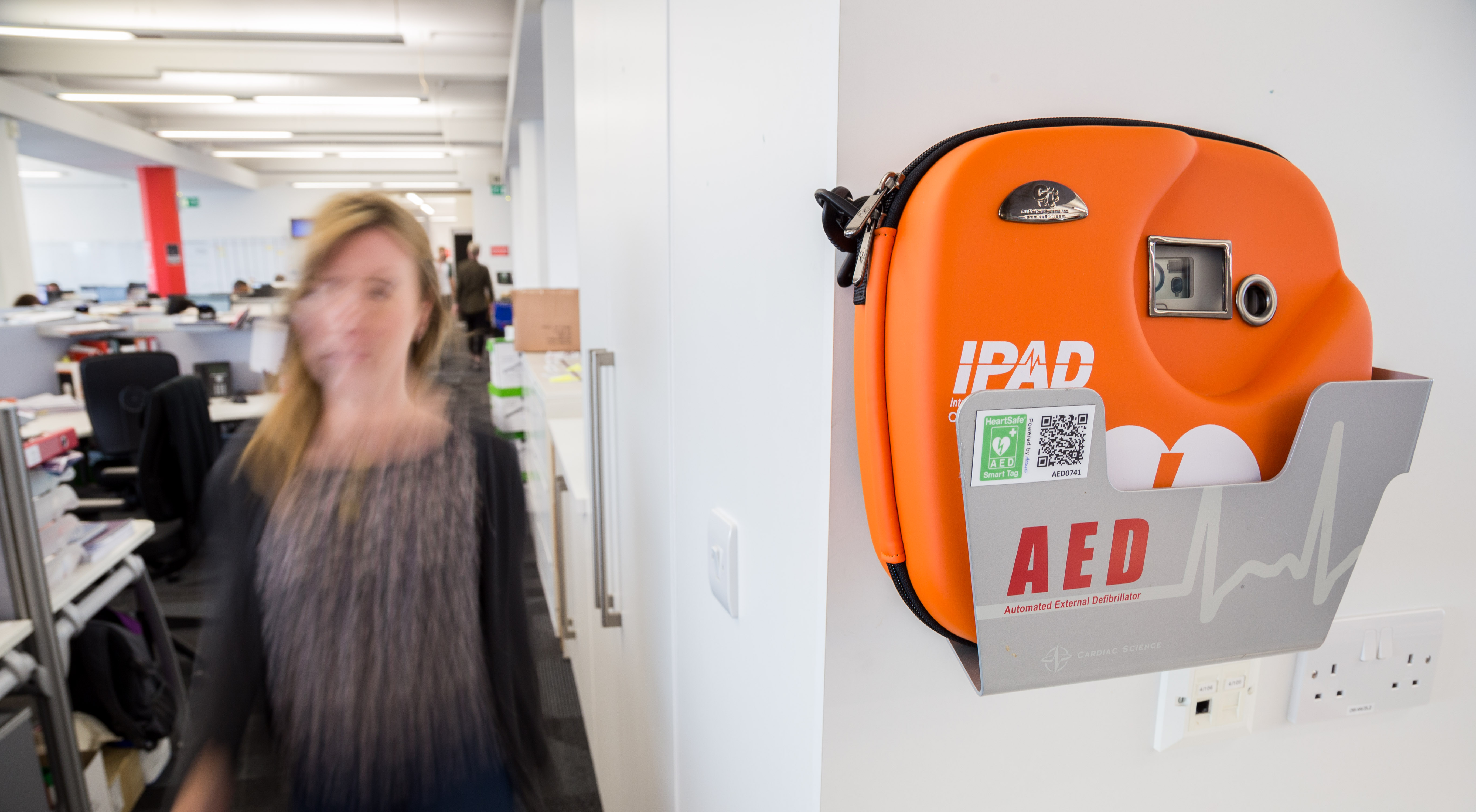 A woman walks past a defibrillator on a wall