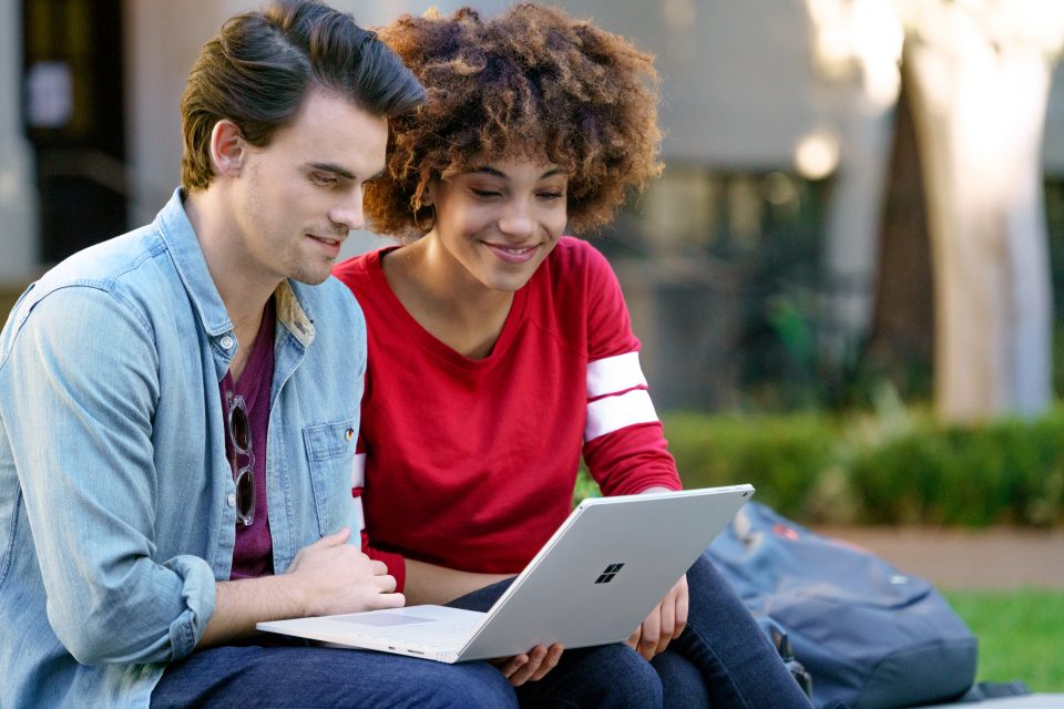 Teenage boy and girl sitting outside at university looking at Surface Book