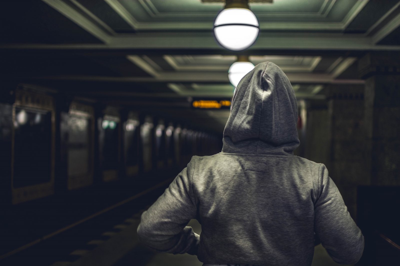 Person wearing hoodie in dark underground train station