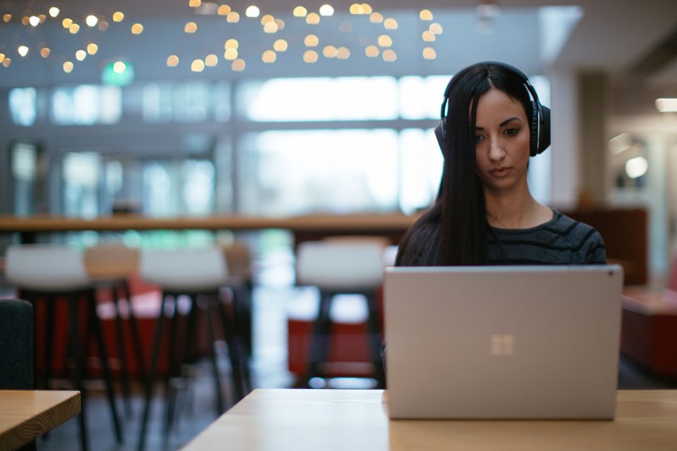 Woman in cafe wearing headphones and using Surface laptop