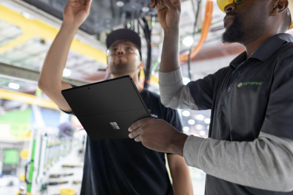 Two male workers in factory, one holding Surface laptop