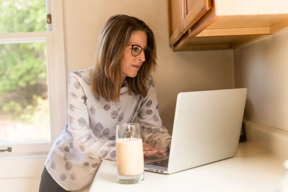 Woman leaning against kitchen worktop using laptop