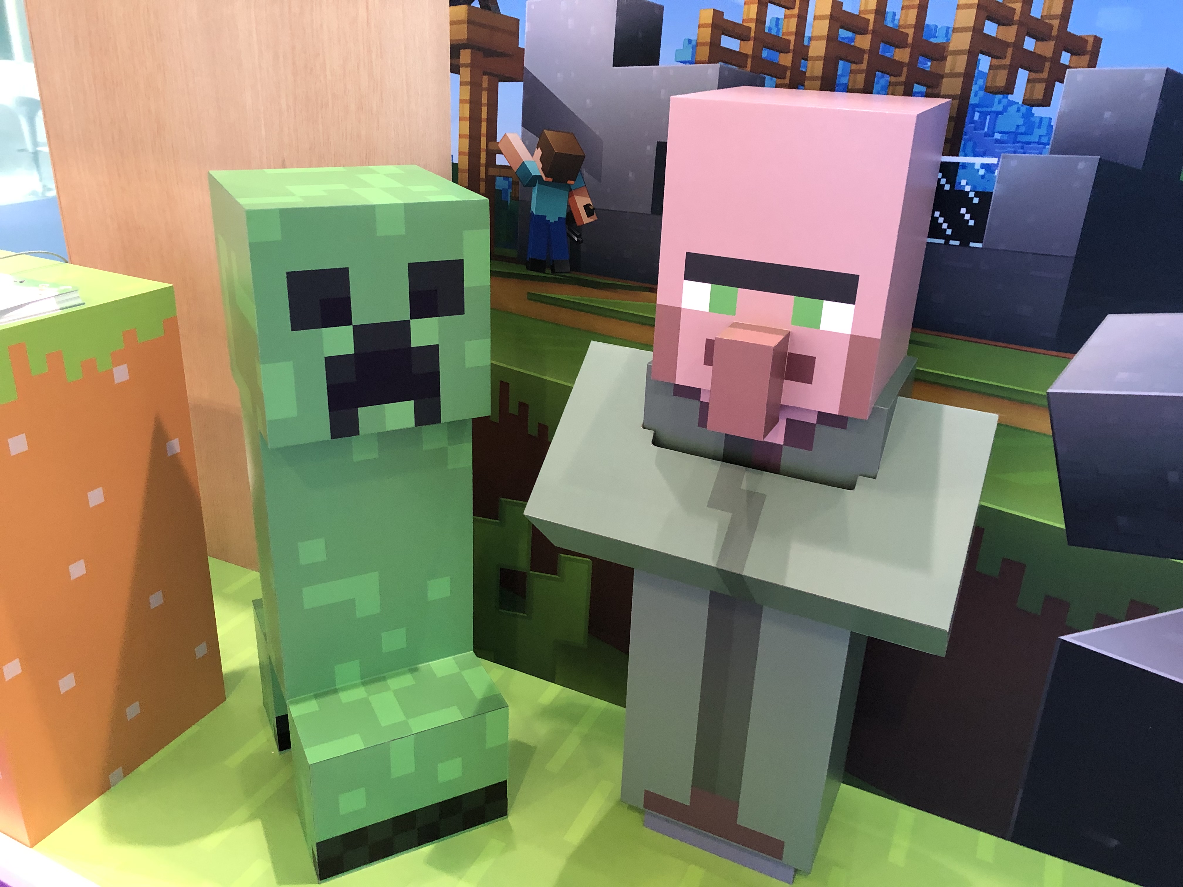 A Creeper and a Villager outside the Minecraft stand