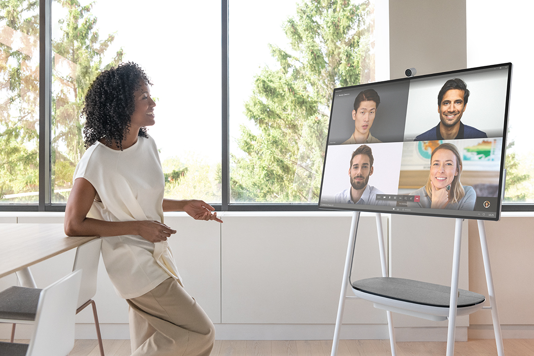 A woman in an office holds a conference call with other team members via Surface Hub 2S