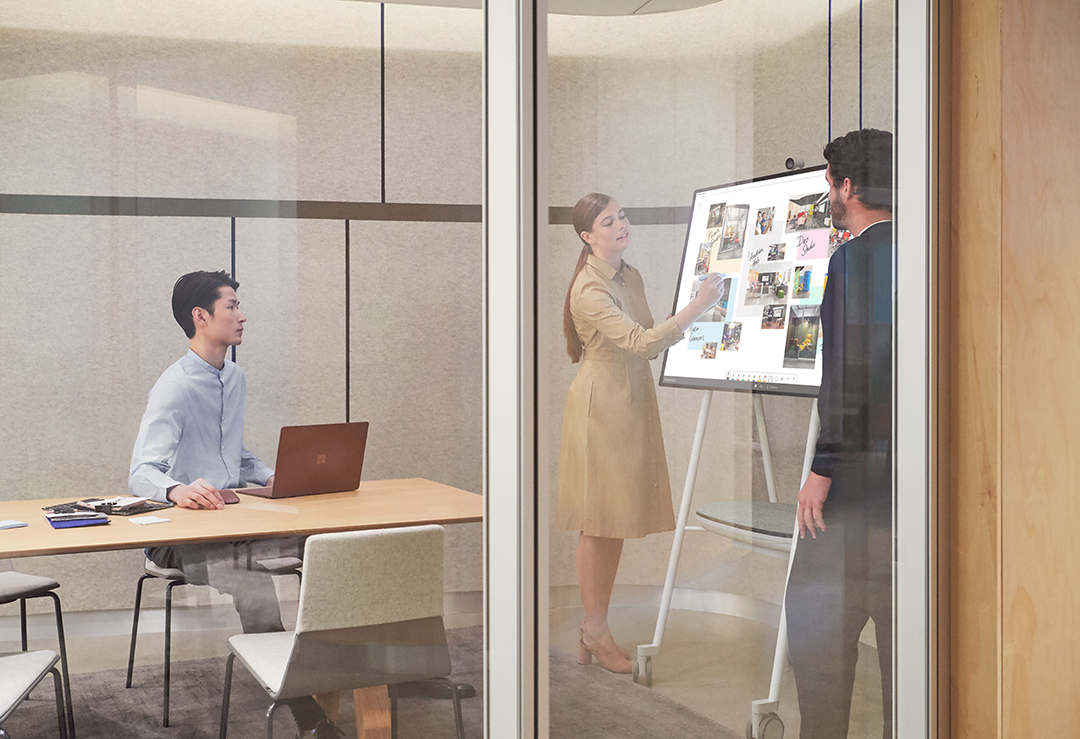A woman uses Surface Hub 2S in an office as two men look on