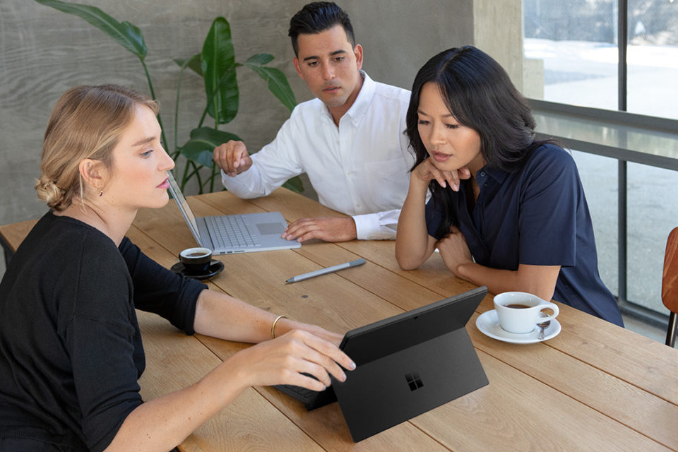 Two women and a man look at a Surface Laptop in the office