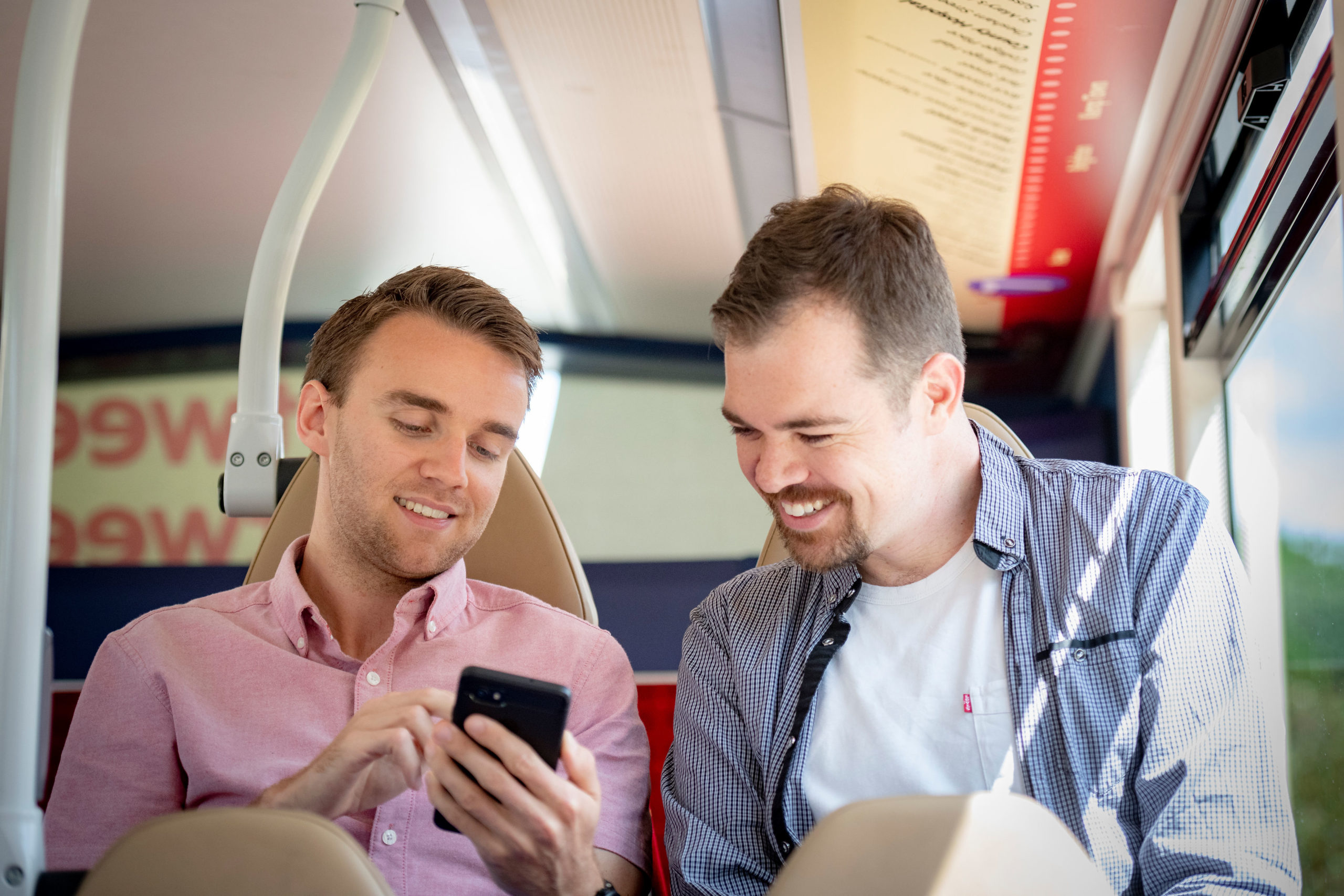 Two male friends on a bus look at a mobile phone