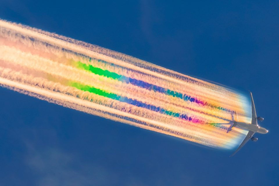 Flying plane with rainbow contrails