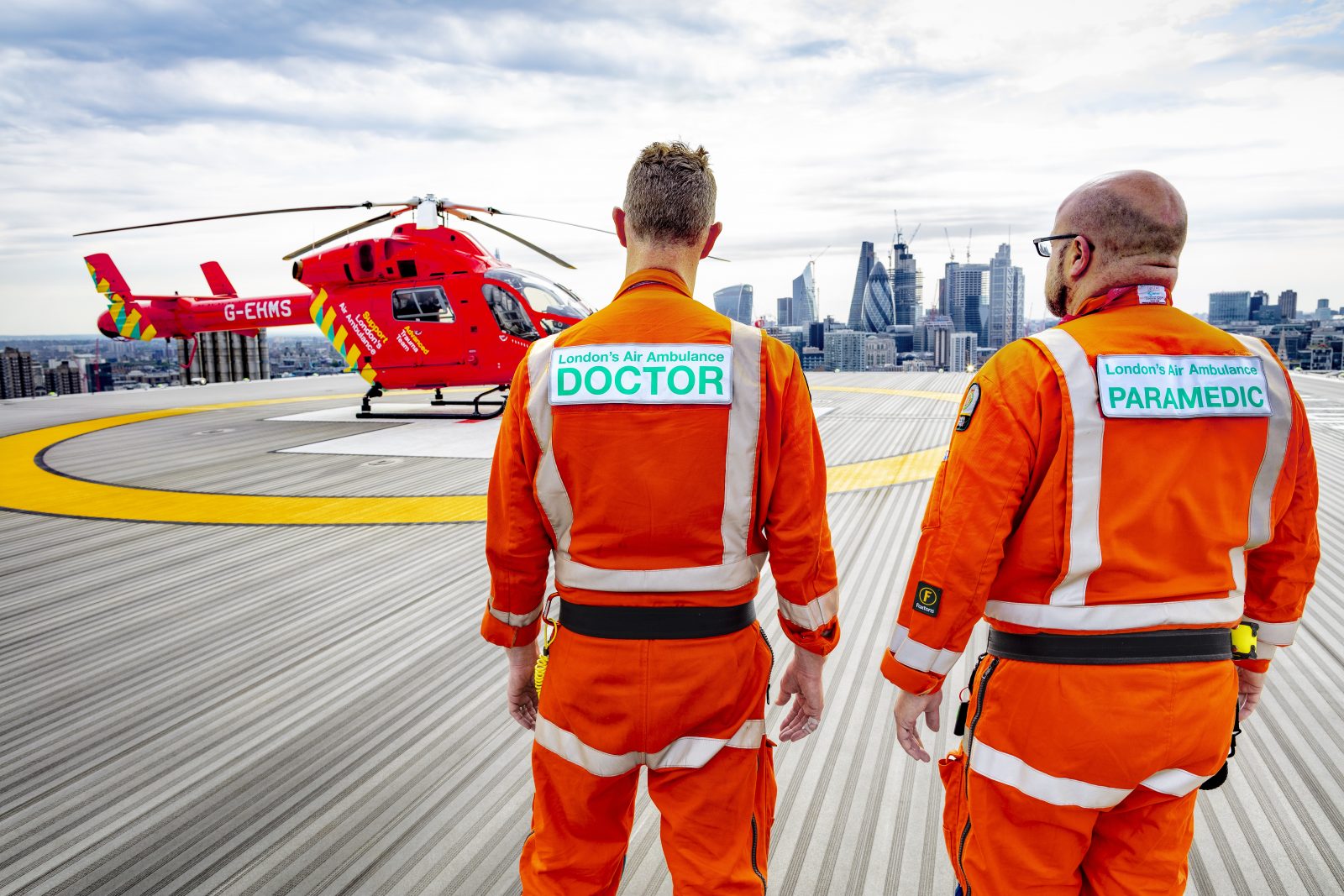 Two paramedics stand on a helipad in front of a helicopter