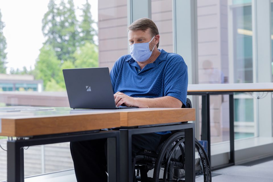A person in a wheelchair uses a Microsoft Surface Laptop at a desk in an office