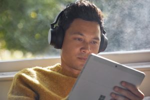 A man wearing headphones works on a Surface device at home