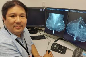 Dr Gerald Lip, lead radiologist at NHS Grampian, beside computer screens displaying scans of mammograms.